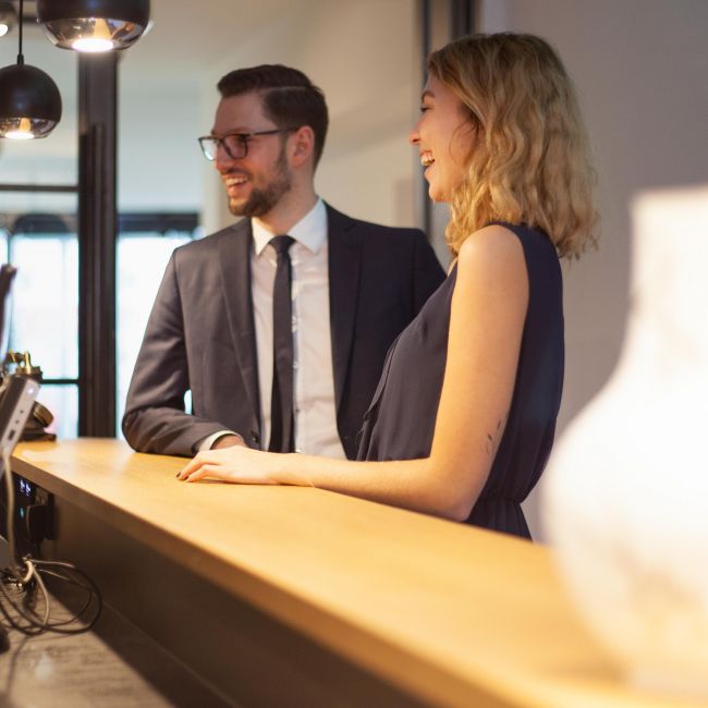 Junges, fröhliches Paar an der Hotelrezeption beim Check-in